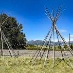 Two sets of teepee poles set up with a blue sky in the background